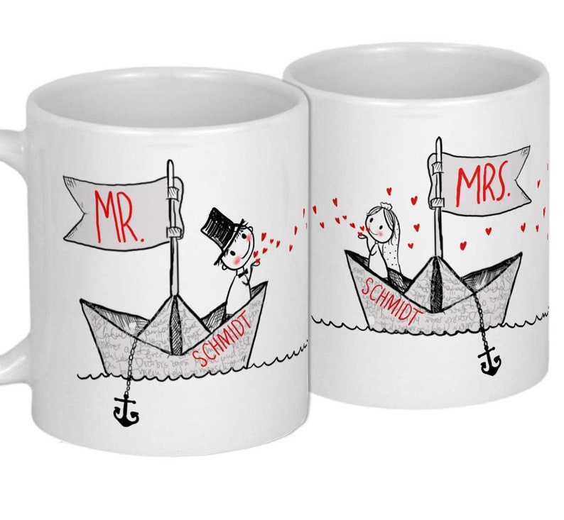 Pu&ograve; includere: Due tazze in ceramica bianca con illustrazioni in nero e rosso di una coppia in barche di carta. Il testo "MR." e "MRS." &egrave; sulle bandiere delle barche. Il testo "SCHMIDT" &egrave; sul fondo di ogni barca. La coppia si sta mandando cuori.
