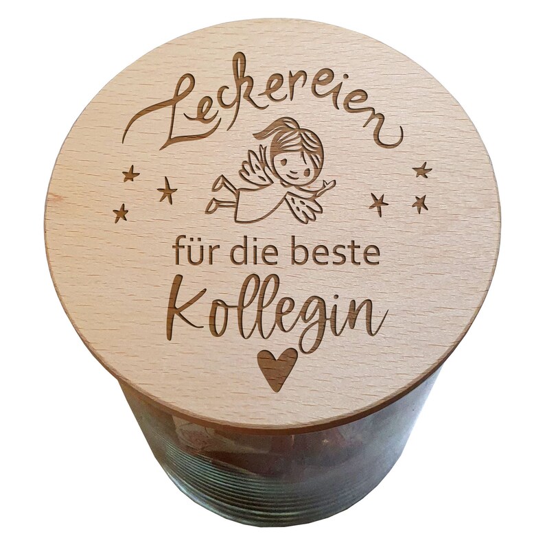 May include: A glass jar with a wooden lid. The lid is engraved with the word "Leckereien", an angel illustration, stars, the phrase "f&uuml;r die beste Kollegin", and a heart. The jar appears to be filled with a dark substance.