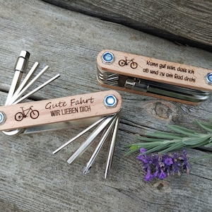 Könnte beinhalten: Zwei Holz-Multitools mit Fahrrad-Design und graviertem Text. Das obere Werkzeug lautet "Kann gut sein, dass ich ab und zu am Rad dreh". Das untere Werkzeug lautet "Gute Fahrt WIR LIEBEN DICH".
