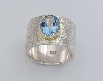 14 mm wide silver ring chiseled with blue topaz 10 x 8 mm and 18kt. Yellow gold setting