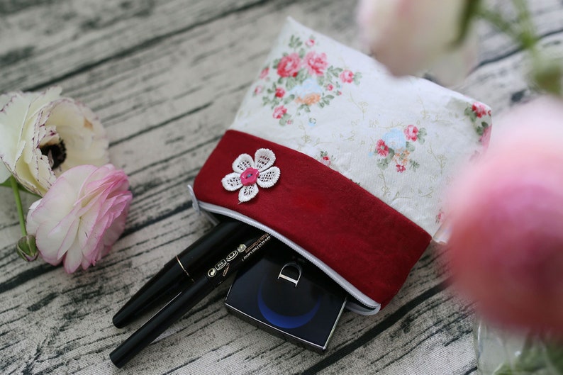 May include: A white and red floral fabric pouch with a zipper closure. The pouch is filled with makeup items, including a black eyeliner and a compact.
