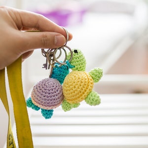 May include: Two crocheted turtle keychains, one yellow and green, the other purple and blue, attached to a yellow lanyard and silver key ring.