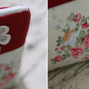 May include: A red and white zippered pouch with a white lace flower and a pink button. The pouch has a floral print on the other side.