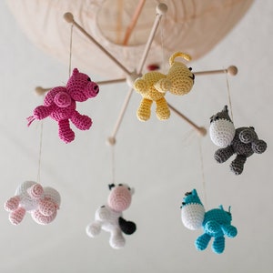 May include: A baby mobile with six crocheted animal toys hanging from a wooden frame. The toys are a pink pig, a yellow dog, a gray cat, a white cow, a pink sheep, and a blue fish.