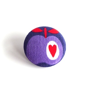 May include: A purple fabric button with a red heart and red leaf design.
