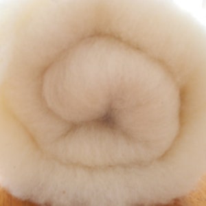Könnte beinhalten: Nahaufnahme eines eng gerollten, cremefarbenen Materials, möglicherweise Watte oder Wolle. Die Textur wirkt weich und flauschig, mit einem Spiralmuster in der Mitte. Das Material wird wahrscheinlich für Bastelarbeiten oder Polsterungen verwendet.