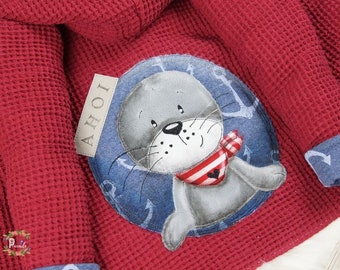 May include: Red waffle knit fabric with a gray seal applique wearing a red and white striped scarf. The seal is surrounded by blue anchors and the text "AHOI" is on a white tag.