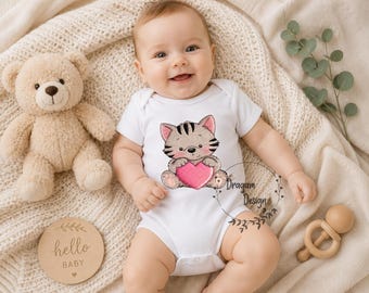 May include: A baby wearing a white onesie with a cartoon cat holding a pink heart. A beige teddy bear, a wooden disc with "hello BABY" text, and a wooden teether are also in the image. The baby is lying on a cream-colored blanket.