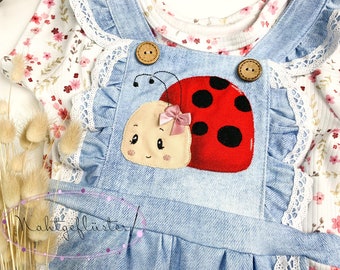 May include: A light blue denim overall dress with white lace trim and a red ladybug applique. The ladybug has black spots and a pink bow.