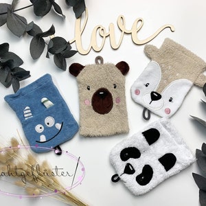 Pode incluir: Quatro toalhas de banho com rostos de animais. As toalhas são bege, azul, branco e marrom. Os animais são um urso, um veado, um monstro e um panda. As toalhas estão penduradas em um fundo branco.