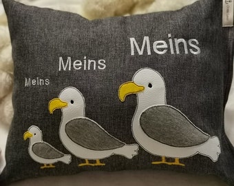 May include: A gray pillow with the word "Meins" embroidered on it three times. The pillow features three white seagulls with yellow beaks and gray wings.