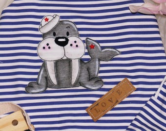 May include: A blue and white striped fabric with a gray and white cartoon walrus wearing a red and white sailor hat. The walrus has a brown leather tag that says "LOVE" on it.
