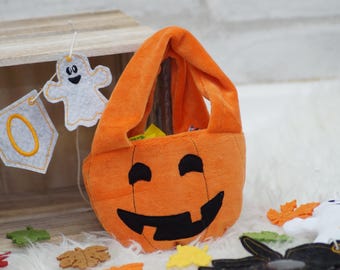May include: Orange felt pumpkin trick-or-treat bag with a black smiling face. The bag has a handle and is filled with candy.