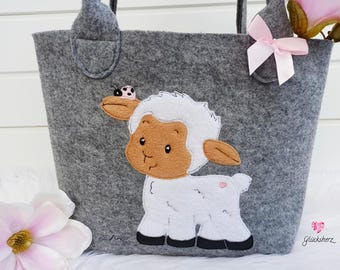 May include: Gray felt tote bag with a white lamb applique and a pink ladybug. The lamb has brown eyes and a pink spot on its side. The bag has a pink bow on the handle and the text "Glückshertz" on the bottom.