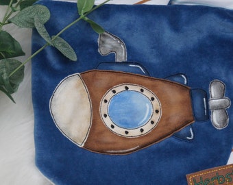 May include: A blue fabric with a brown and white submarine applique. The submarine has a round window with a blue center and a black outline.