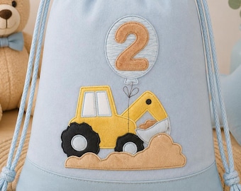 May include: A light blue drawstring backpack featuring an embroidered yellow construction excavator, a pile of brown dirt, and a circular patch with the number 2 inside a balloon shape. The bag has matching light blue cord straps.