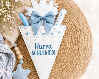May include: A white cone-shaped gift holder featuring a blue bow, a star-patterned border, and the embroidered text Hurra SCHULKIND! in blue. The item contains a blue pen and a star-patterned tube, with a star-shaped charm attached by beads.
