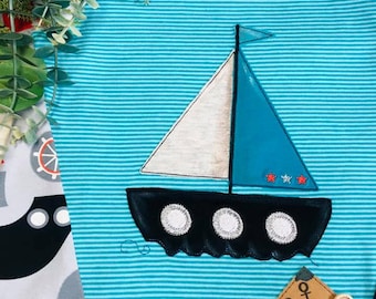 May include: A turquoise blue striped long-sleeved shirt with a white and blue sailboat applique. The sailboat has a black hull with three white circles and a red star on the sail. The shirt has a brown fabric anchor patch with white stitching.