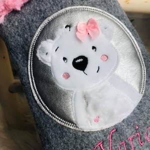 May include: Grey felt stocking with a silver circle applique featuring a white polar bear with a pink bow. The stocking is personalised with the name "Varia" in pink thread.