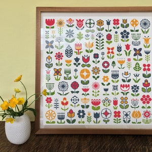 May include: A framed cross-stitch pattern featuring a variety of colorful flowers in a white background. The flowers are in a variety of styles, including tulips, daisies, and other floral designs.