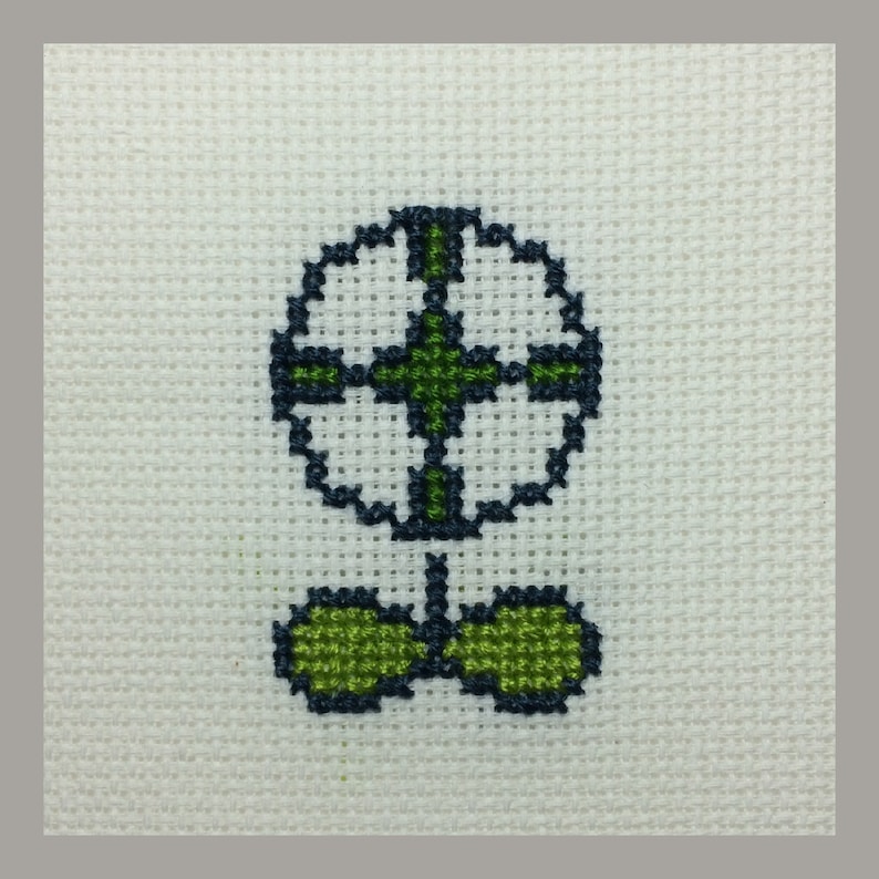 May include: A white cross-stitch embroidery of a green flower with a dark blue outline.