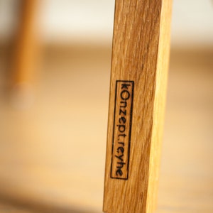 May include: Close-up of a wooden chair leg with a black label that reads "Konzept:rehye" and a gray felt pad on the bottom.
