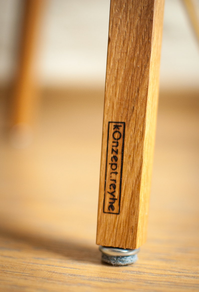 May include: Close-up of a wooden chair leg with a black label that reads "Konzept:rehye" and a gray felt pad on the bottom.
