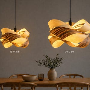 May include: Two pendant lights with a unique design. The lampshades are made of layered wood, with a warm, natural color and a darker, striped pattern. The larger lamp is 60 cm in diameter, and the smaller one is 44 cm in diameter. The lights hang above a wooden dining table.