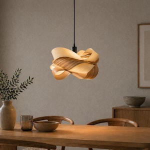 May include: A modern pendant light with a layered, organic design. The light fixture is made of light and dark wood tones, suspended from a black cord. The light hangs above a wooden dining table.