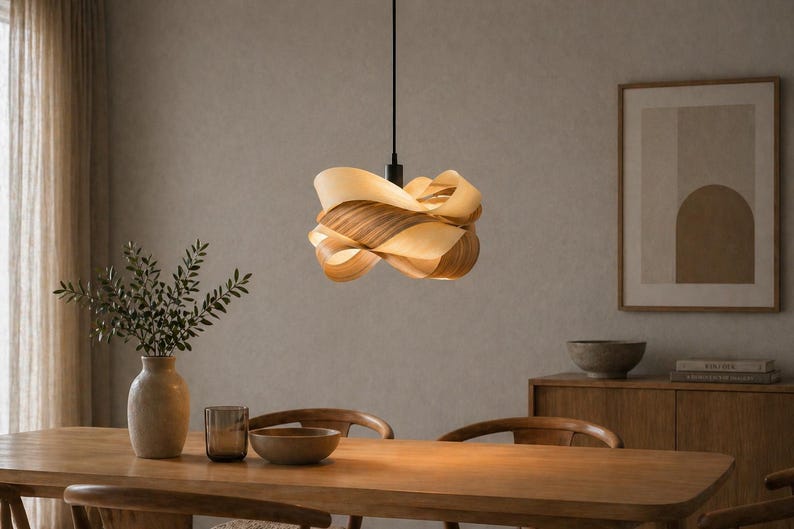 May include: A modern pendant light with a layered, organic design. The light fixture is made of light and dark wood tones, suspended from a black cord. The light hangs above a wooden dining table.