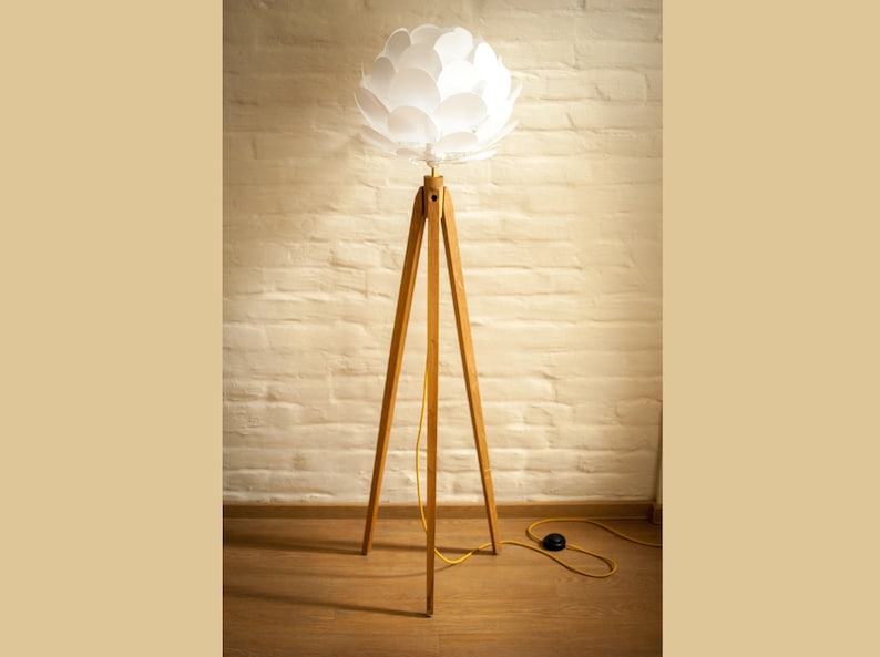 May include: A white, flower-shaped lampshade sits atop a wooden tripod floor lamp with a yellow cord.