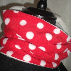 Könnte beinhalten: Roter Fleece-Halswärmer mit weißen Punkten. Der Halswärmer ist gefaltet und auf einer Puppe ausgestellt.