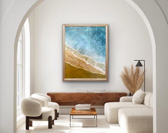 May include: A framed abstract painting of a beach scene with blue and green water and a sandy shore. The painting is in a modern living room setting with a couch, chairs, and a coffee table.