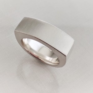 Op de afbeelding: Een zilveren ring met een vierkante band. De band is glad en heeft een geborstelde afwerking.