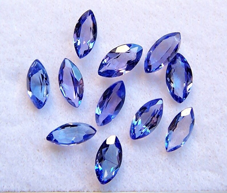 May include: A collection of twelve marquise-shaped blue gemstones, likely sapphires or topaz, displayed on a white surface.