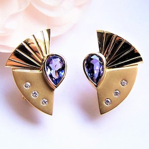 May include: A pair of gold earrings with a fan-shaped design and a purple gemstone in the center. Each earring has three small diamonds on the bottom.