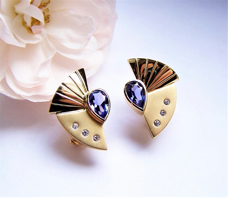 May include: A pair of gold earrings with a fan-shaped design and a teardrop-shaped blue gemstone in the center. Each earring has three small diamonds around the gemstone.