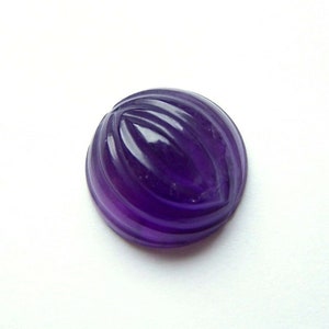 May include: A carved amethyst cabochon gemstone with a purple hue. The gemstone has a rounded shape and a smooth, polished surface.