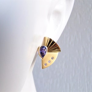 May include: Gold earrings with a purple gemstone and three small diamonds. The earrings have a fan-shaped design.