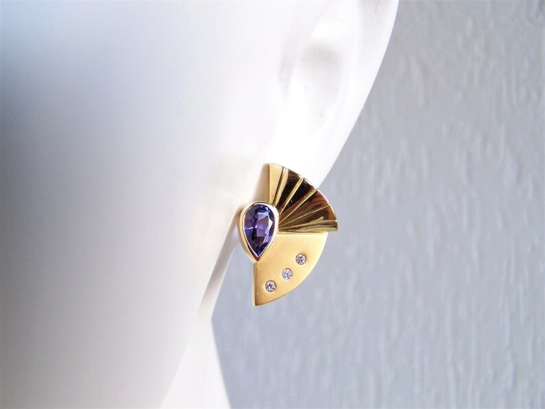 May include: Gold earrings with a purple gemstone and three small diamonds. The earrings have a fan-shaped design.