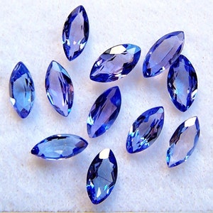 May include: A collection of twelve marquise-shaped blue gemstones. The gemstones are faceted and have a light blue to dark blue color.