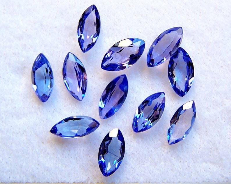 May include: A collection of twelve marquise-shaped blue gemstones. The gemstones are faceted and have a light blue to dark blue color.