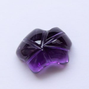 May include: A deep purple amethyst gemstone carved into a flower shape. The gemstone is faceted and has a smooth, polished finish.