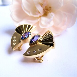 May include: A pair of gold earrings with a purple gemstone and small diamonds. The earrings are shaped like a fan.
