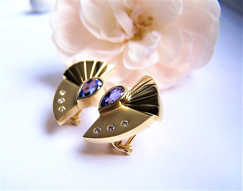 May include: A pair of gold earrings with a purple gemstone and small diamonds. The earrings are shaped like a fan.