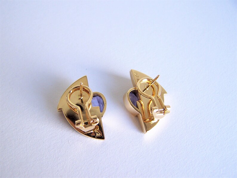May include: A pair of gold tone earrings with purple stones. The earrings are shaped like a crescent moon and have a hinged closure.