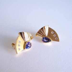 May include: A pair of gold earrings with a fan-shaped design. Each earring features a purple gemstone and three small diamonds.