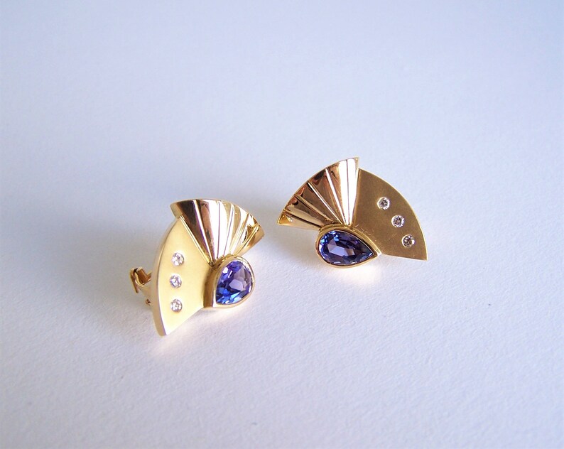 May include: A pair of gold earrings with a fan-shaped design. Each earring features a purple gemstone and three small diamonds.