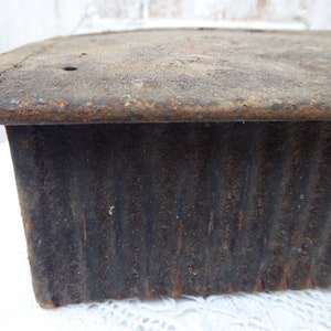 May include: A vintage, dark grey metal loaf pan with a corrugated exterior and a slightly rusted top edge.