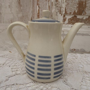 May include: A white ceramic teapot with a blue and white geometric pattern. The teapot has a lid and a spout.